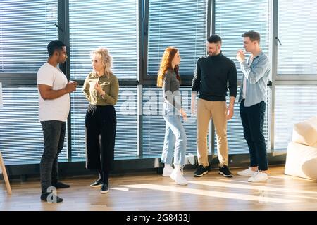 Front view of young multiethnic coworkers having fun conversation during coffee break in modern office. Stock Photo