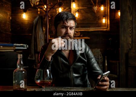 Bearded man wearing suit and drinking whiskey brandy or cognac. Sommelier tastes alcohol drink. Degustation and tasting. Portrait of young man holding Stock Photo