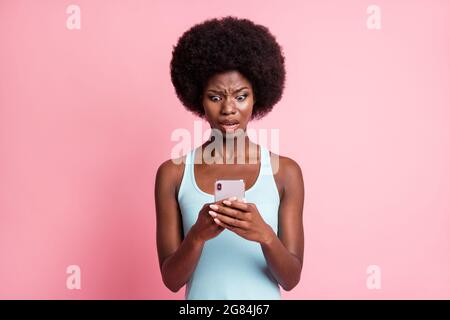 Photo of shocked brunette upset dark skin young woman hold phone read sms isolated on pink color background Stock Photo