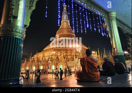 21.01.2014, Yangon, Myanmar, Asia - Buddhist monks sit in front of the illuminated stupa of the gilded Shwedagon Pagoda in the evening. Stock Photo