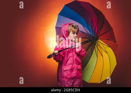 Cute little boy are preparing for autumn rain day. Cheerful boy in raincoat with colorful umbrella. Kid in rain. Sale for entire autumn kids Stock Photo