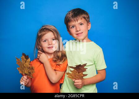 Little girl and cute boy are preparing for autumn kids sale day. Child isolated on blue background board for Copyspace. Happy autumn people concept Stock Photo