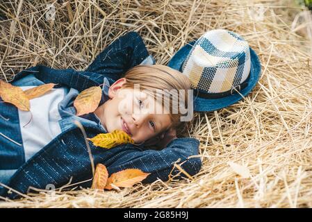 Happy child at the autumn fair. Fair-haired kid playing with leaves and looking at camera. Little boy advertises natural products. The boy advertises Stock Photo