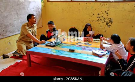 teacher with disabilities (without legs), eagerly teaches his students at a school Stock Photo