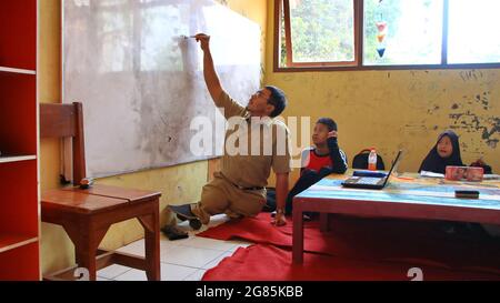 teacher with disabilities (without legs), eagerly teaches his students at a school Stock Photo