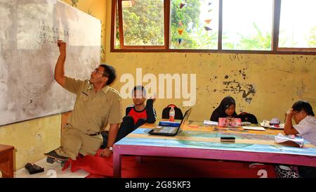 teacher with disabilities (without legs), eagerly teaches his students at a school Stock Photo