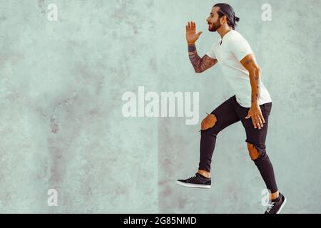 Crazy young man jumping in casual white t-shirt posing isolated on grey wall background. People lifestyle concept. Copy space. Stock Photo