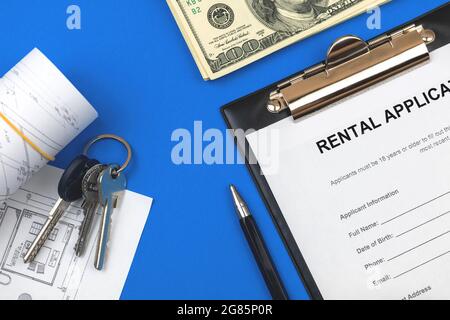 Office desktop with rental appliaction form. Financial and property concept. House keys, pen and money on a blue background. Top view Stock Photo