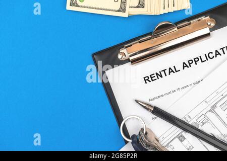 Rental agreement on clipboard. Office desktop with contract, money, house keys and pen. Blue background, top view Stock Photo