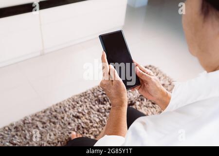 senior woman using mobile phone while sitting on sofa at home Stock Photo