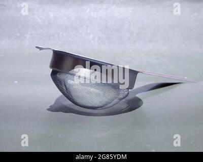 aluminium metal tea filter kept on gray surface, kitchen cutlery product image. Stock Photo