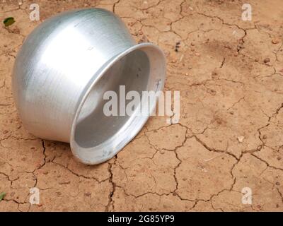 Silver metal food bowl lying on dry dehydrated soil filed, kitchen cutlery product image. Stock Photo