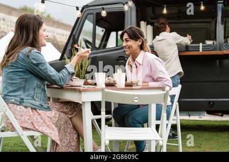 Happy mature women having fun eating in a street food truck outdoor Stock Photo