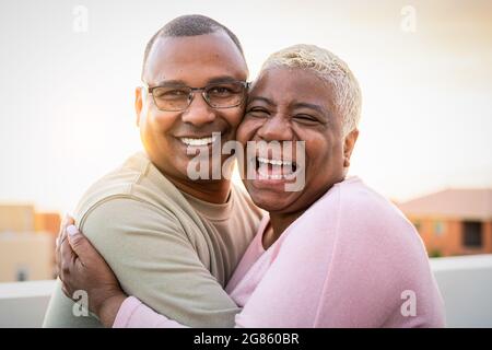 Happy Latin senior couple having romantic moment embracing on rooftop during sunset time - Elderly people love concept Stock Photo