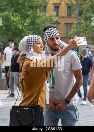 Arab-looking Boy and Girl who are Using a Smartphone to take a Picture of Themselves in Public Square. Stock Photo