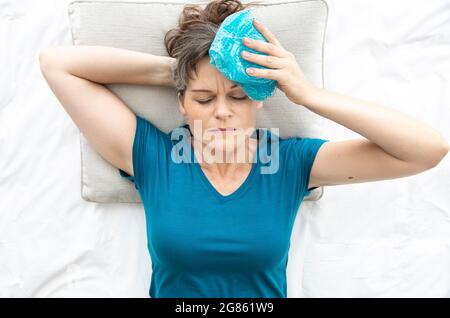 Midlle aged woman holding icebag on her head to alliviate pain Stock Photo