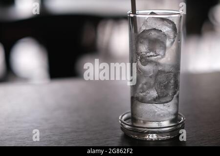 A glass full of partially melted ice cubes, with a drinking straw, on a wooden table in coffee-shop Stock Photo