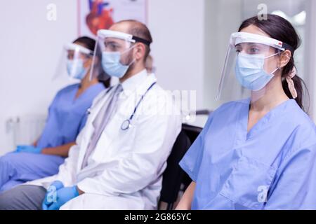 Portrait of medical staff in uniform and protective mask looking at camera. Team of professional medicine workers in safety mask posing at camera together sitting in new normal hospital Stock Photo