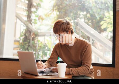 Focused millennial student making notes writing down information from book in cafe preparing for test Stock Photo
