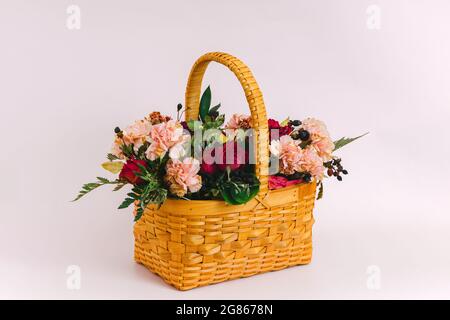 A yellow wicker basket with a bouquet of flowers stands on a delicate pink background. Greeting card. Stock Photo