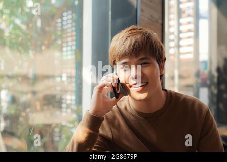 Confident young man talking on the mobile phone and smiling while sitting in cafe Stock Photo