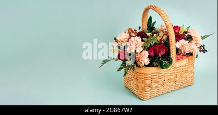 This is a bouquet of delicate flowers in a wicker basket on a blue background of pastel color. Banner for congratulations with space for copying. Summer flowers of calm tones. Stock Photo