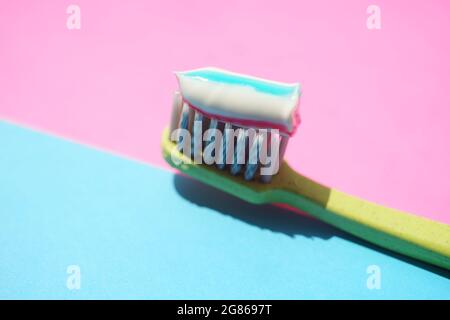 Green plastic toothbrush with striped toothpaste on a pink blue table. Stock Photo