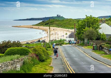 Road down to the village and beach at Low Newton-on-the Sea in Northumberland, with Dunstanburgh Castle in the distance. Stock Photo