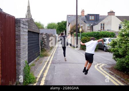 Happy childreh boys brothers rear back view hop skip jump click heels in elation running through a street alley in Cardiff Wales UK 2021 KATHY DEWITT Stock Photo