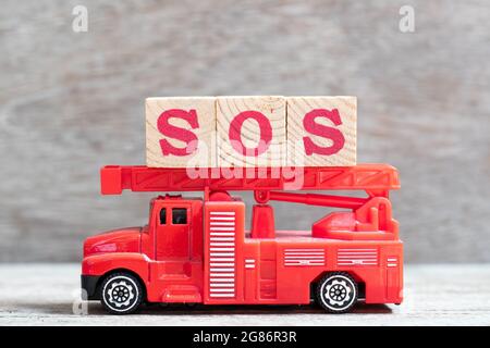 Red fire truck hold letter block in word SOS (abbreviation of save our soul/ship or sibling over shoulder) on wood background Stock Photo