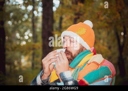 Mature man in jacket suffering from cold. Blowing nose with a tissue, looking miserable unwell very sick. Healthcare and medicine concept - ill man Stock Photo