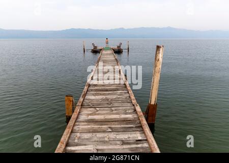 Boy in swimsuit standing on wooden pier at Lake Skadar. Shkodra, Albania Stock Photo