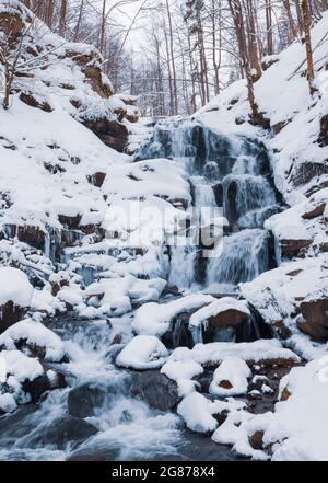 Small waterfall of cold water flow among the stones covered with snow Stock Photo