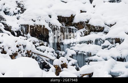 Small waterfall of cold water flow among the stones covered with snow Stock Photo