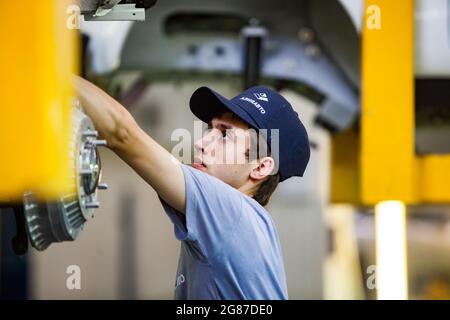 Ust'-Kamenogorsk,Kazakhstan-May 31,2012:Asia-Auto company auto-building plant.Young man assembling car suspension and wheel hub.Blurred yellow hoist. Stock Photo