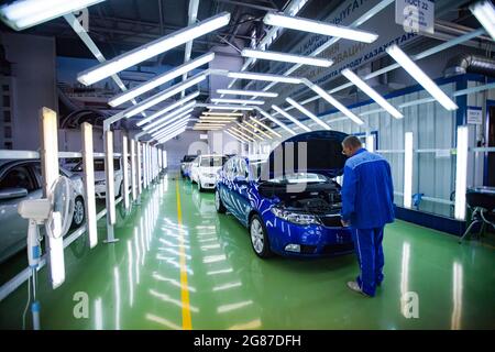Ust'-Kamenogorsk, Kazakhstan: Asia-Auto company auto-building plant. Worker checking painting quality in light tunnel. White car in focus. Stock Photo