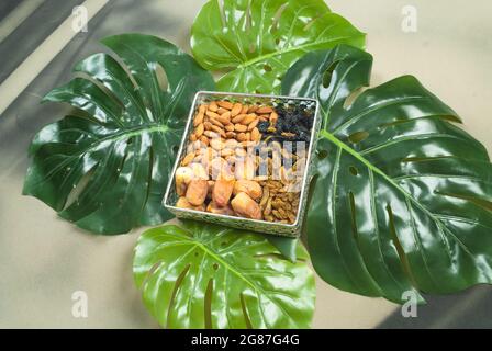 organic healthy food in bowl on tropical leaves,different dry fruits almonds dates dry golden black raisins (kishmish) jim diet Stock Photo
