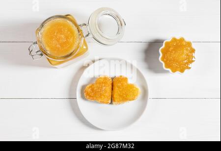 Fruit yellow jam on a white wooden background. Heart shaped delicious toast on a plate. View from above. Stock Photo