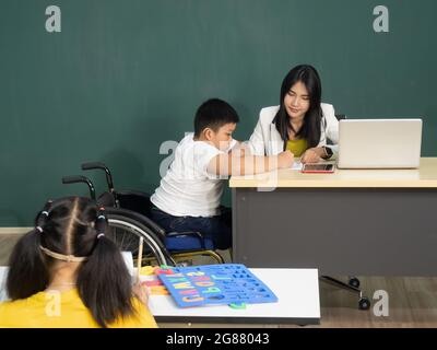 Spacial classroom of disabled kids or autism child learning and painting at a paper with teacher helping in the classroom. Stock Photo