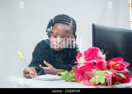 African girl child studying, learning, reading and researching alone for excellence in her education with a laptop, flower and jotter in her front Stock Photo