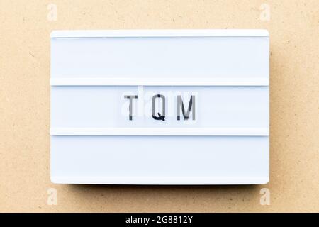 White lightbox with word TQM (Abbreviation of total quality management) on wood background Stock Photo