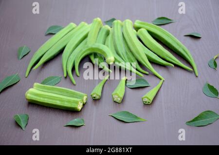 closeup the bunch ripe green ladyfinger sliced with leaves on the brown background. Stock Photo