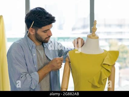 Fashion designer room. The men's dressmaker using tape measure measuring the shoulder size of dress on the mannequin. Stock Photo