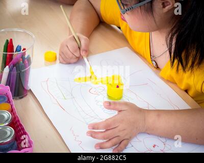 The cute little girl down syndrome learning about drawing and painting while enjoying development exercises at home. Education and special child conce Stock Photo