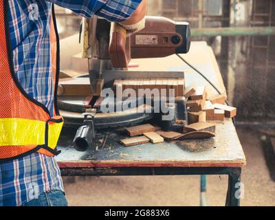 The carpenter craftsman wearing safety gear working with hardwood using a miter saw to cut a piece of wood in the workshop. Manufacture of wood produc Stock Photo