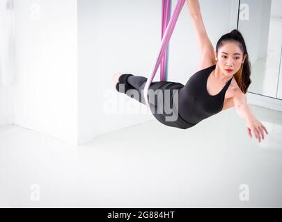 Young beautiful Asian dancer dressed in black color performing aerial dance with multi-color fabrics in the studio. Stock Photo