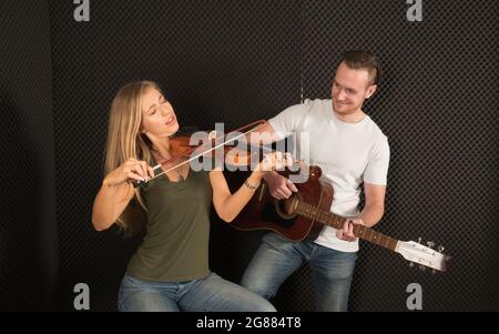 Portrait of a handsome man musician plays the guitar, a beautiful woman musician plays the violin in the recording studio. Stock Photo