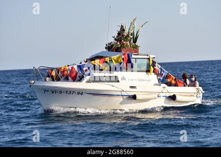 A view of a boat leading with a statue of the Virgen del Carmen during the seafaring procession in Vendrell. Every year on July 16 a religious festival is celebrated in honor of the Virgen del Carmen, patron saint of sailors and fishermen, although the celebration is on July 16, the procession is held on the weekend so that more people can attend the celebration. The statue of Virgin, is carried by a group of people taking it to a boat leaving during the procession through the waters of the sea near the port followed by several boats. Stock Photo