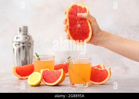 Woman squeezing grapefruit into glass on light background Stock Photo
