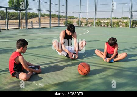 Three brothers doing leg stretching exercises. Siblings stretching before playing basketball. Stock Photo
